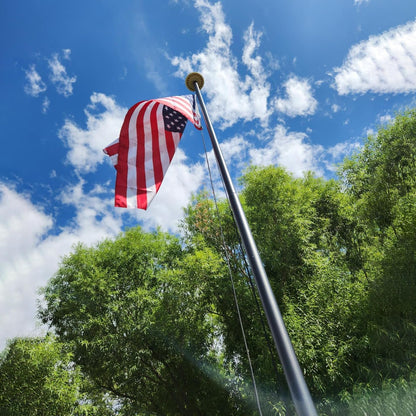 American flag on a pole against a blue sky with clouds and green trees.