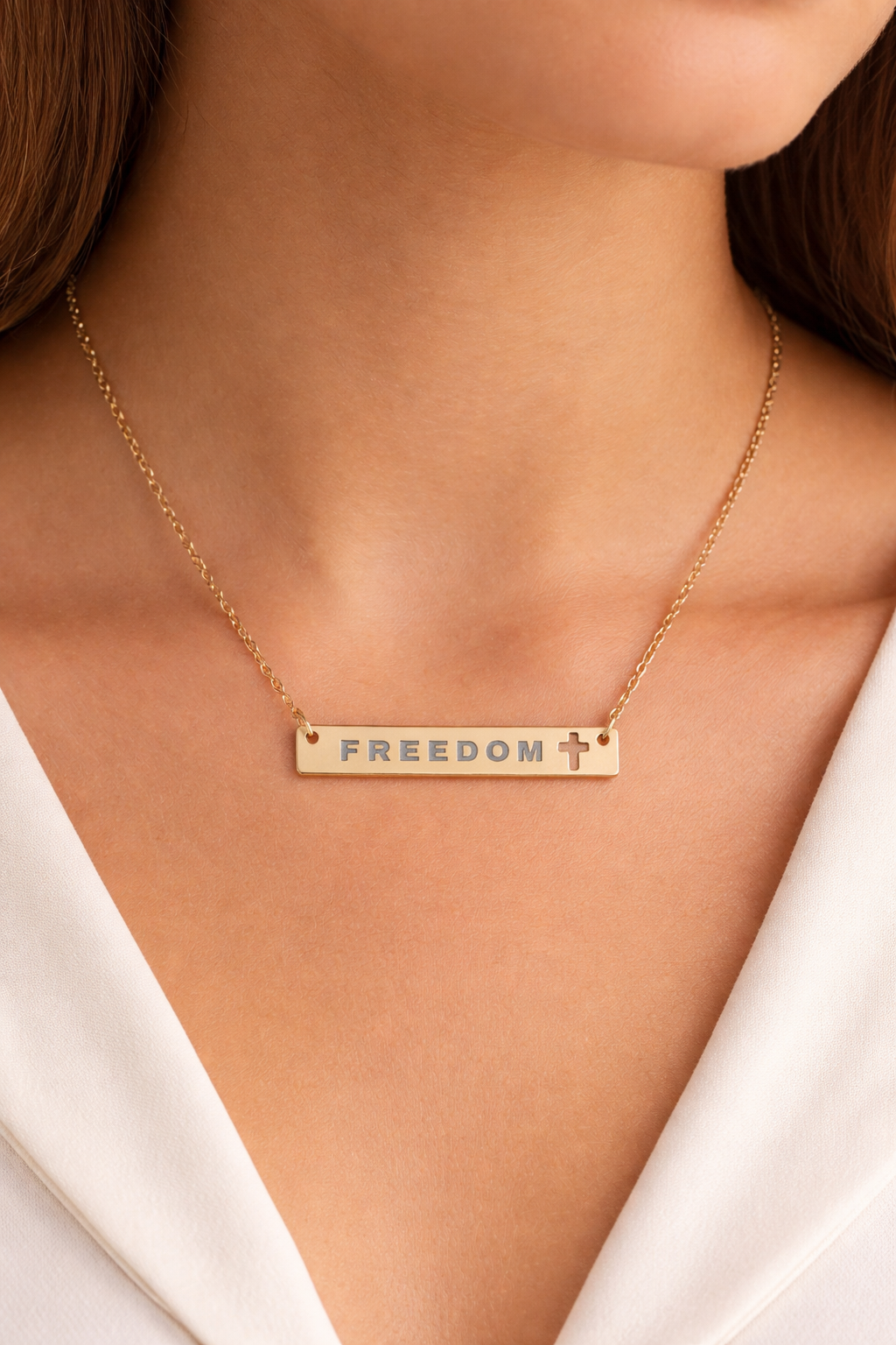 Gold necklace with 'FREEDOM' pendant on a person wearing a white top