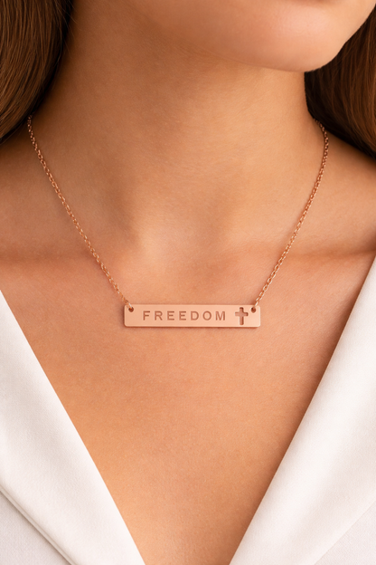 Rose gold necklace with 'FREEDOM' pendant on a person wearing a white top.