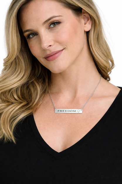 Woman wearing a necklace with a 'FREEDOM' pendant on a plain background