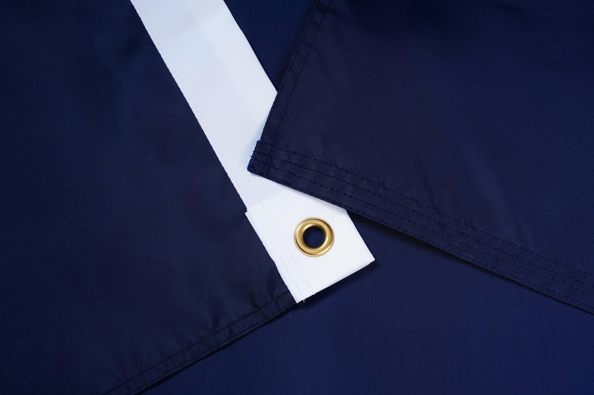 Close-up of navy blue fabric with a white stripe and gold grommet.