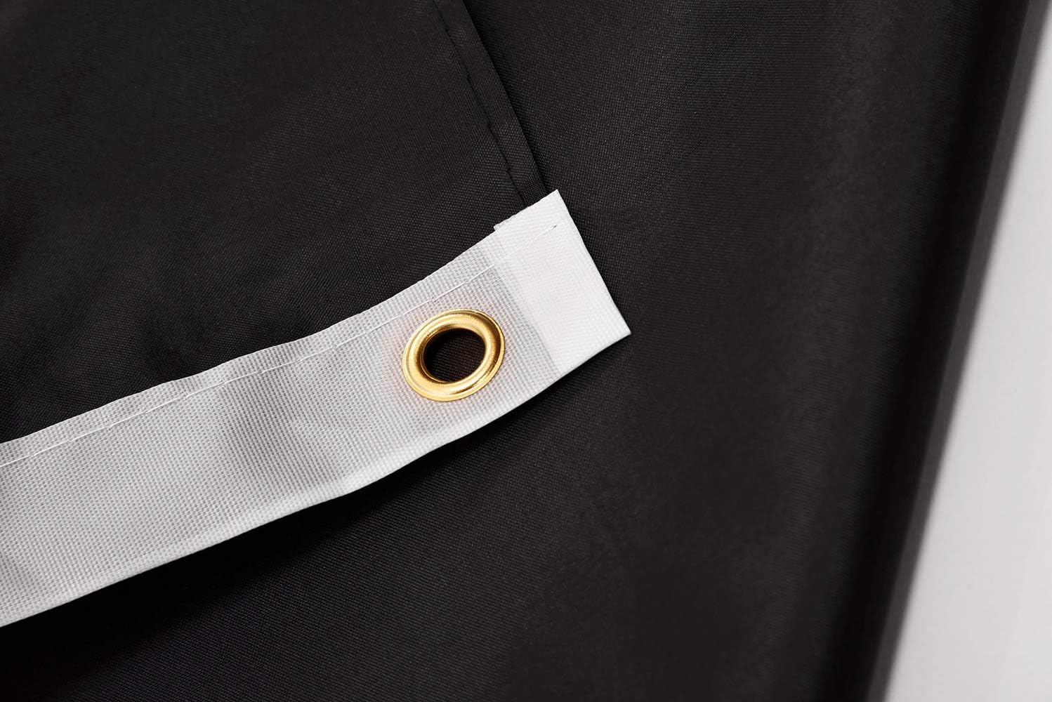 Close-up of a black fabric with a gold eyelet on a white strip.
